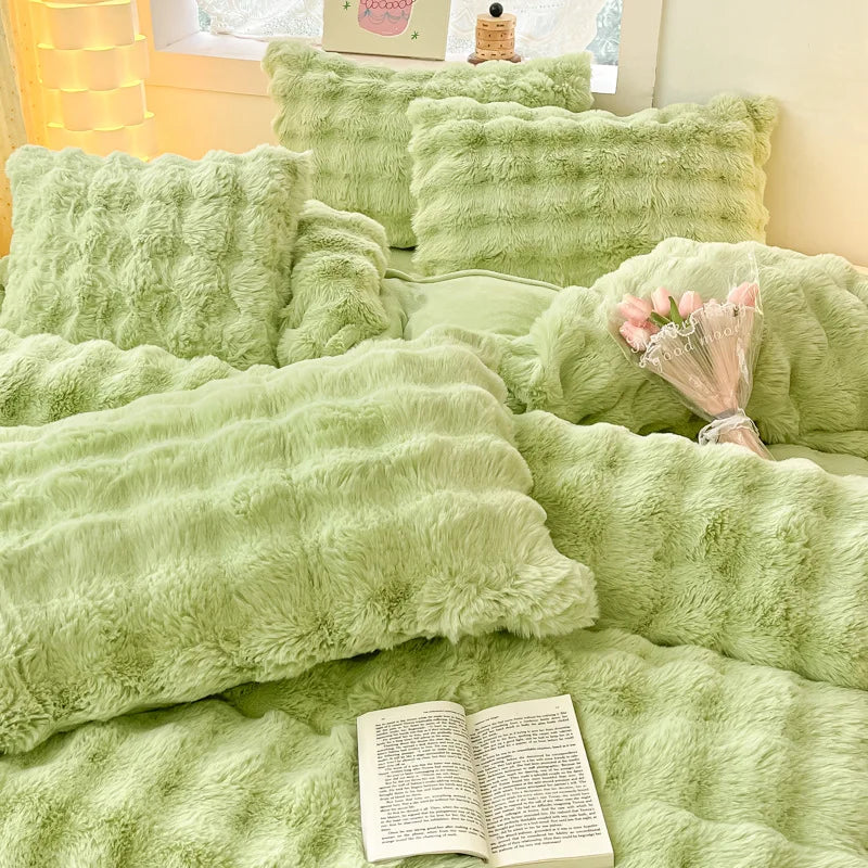 A collection of soft, light green faux fur bedding including pillows and a blanket.