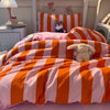 A bed decorated with an orange and pink striped duvet cover set featuring a stuffed animal pillow.