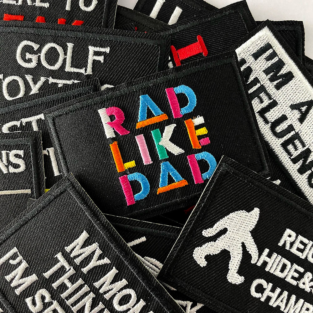 A collection of black embroidered iron-on patches featuring text like RAD LIKE DAD and other humorous phrases.