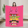 A pink throw blanket featuring a cartoon illustration of a stylized, multi-headed character.