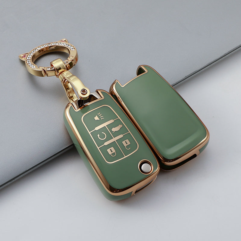 A gold-toned TPU key fob cover in olive green with a keyring, resting on a gray surface.