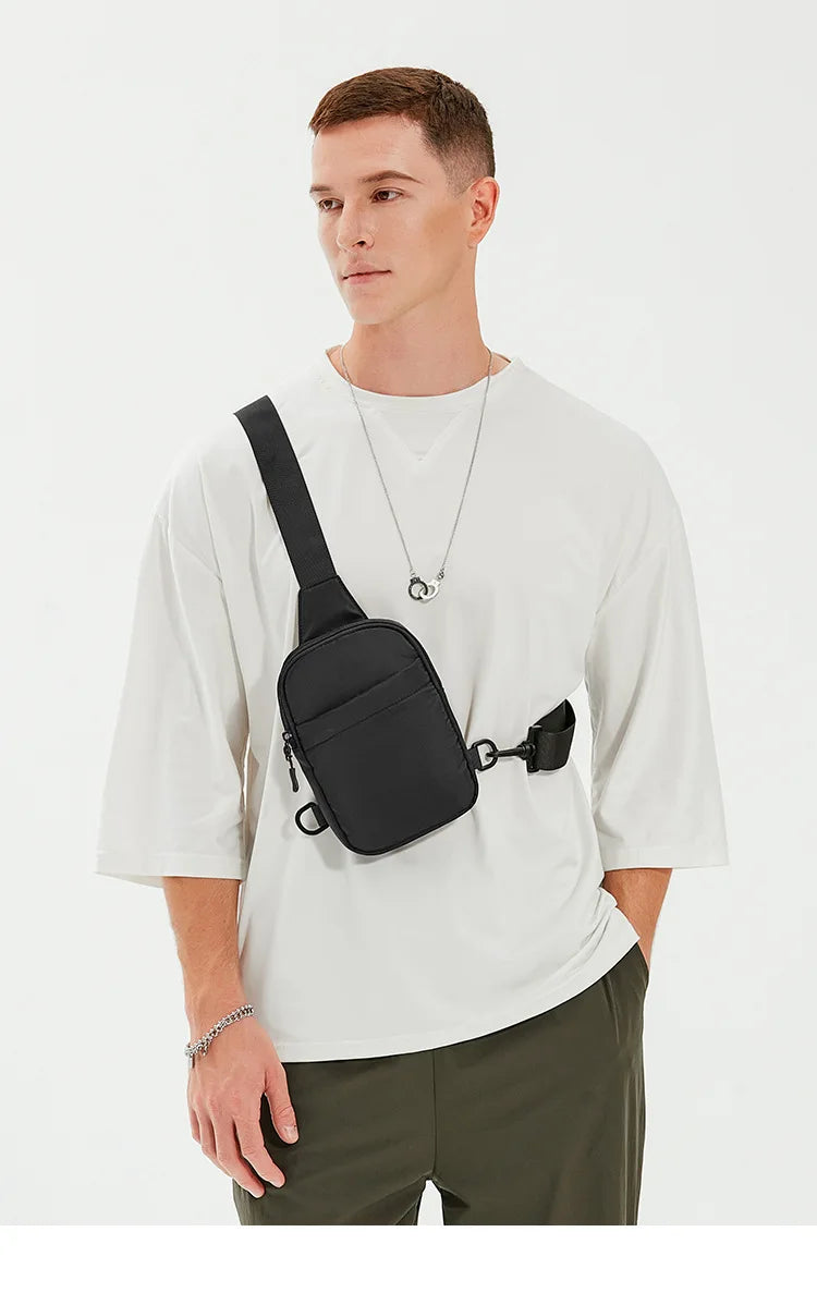 A male model wearing a white t-shirt and olive pants, holding a black 2-in-1 convertible sling bag.