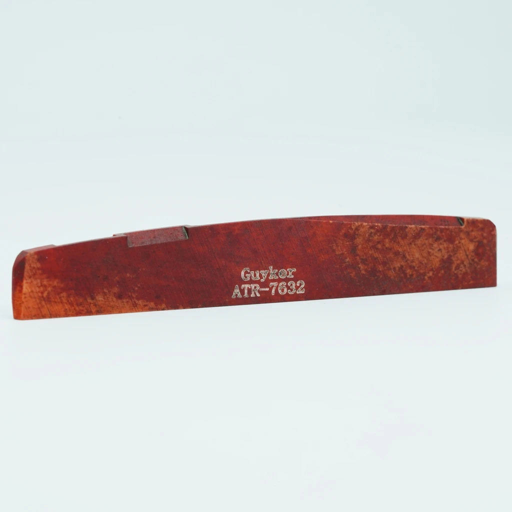A wooden acoustic guitar bridge saddle with the text Guykor ATR-7632 engraved on it.
