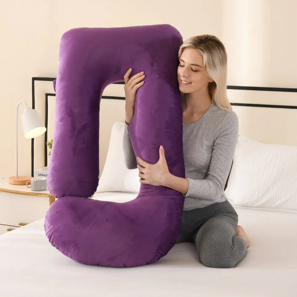 Une femme serre un oreiller de maternité violet en forme de G sur un lit blanc.