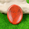 A smooth, oval, reddish-orange natural crystal stone resting on green grass, held by a hand.