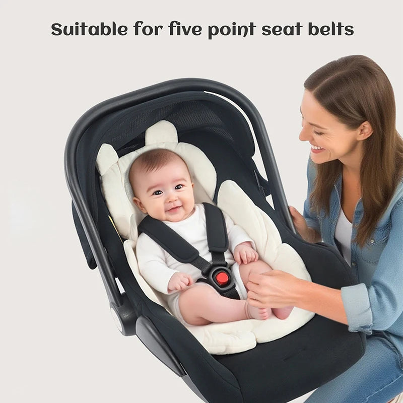 A woman is adjusting a baby in a black stroller seat cushion designed for five-point seat belts.