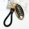 A gold and black key fob with a braided leather strap is shown against a light background.
