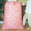 A pink drawstring laundry bag with a pattern of small red and green leaves is being held by a person.