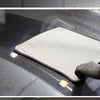A microfiber car drying towel is being used to dry a car surface, with a small yellow cleaning tool visible.