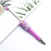 A purple ballpoint pen with a sparkly pink and purple sequin section is shown against a white background.
