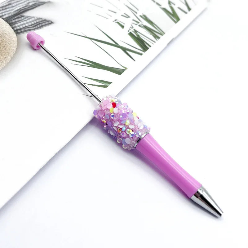 A purple ballpoint pen with a sparkly pink and purple sequin section is shown against a white background.