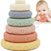 An 8-piece set of soft silicone stacking rings in various pastel colors stacked on a white background next to a baby's hand.