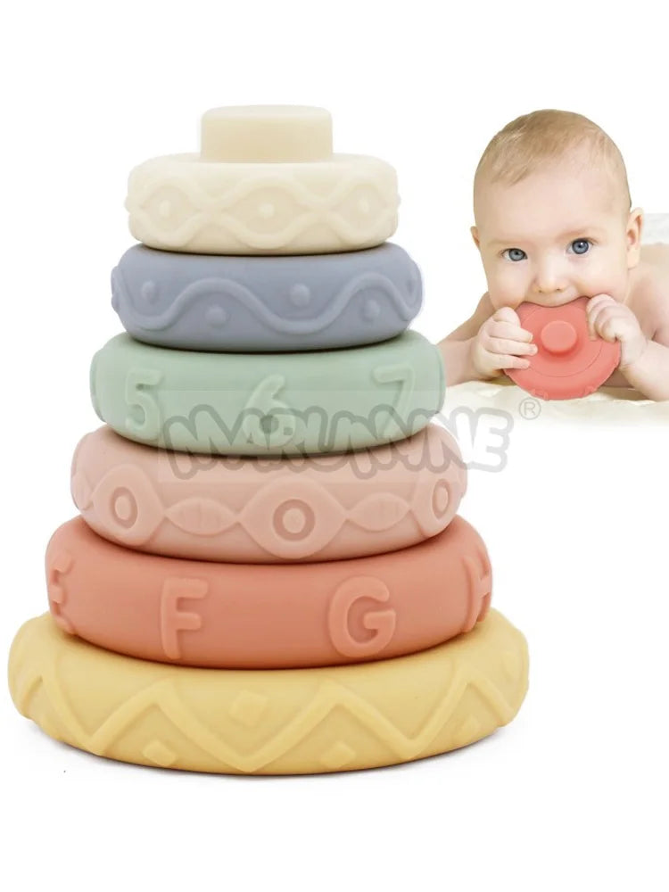 An 8-piece set of soft silicone stacking rings in various pastel colors stacked on a white background next to a baby's hand.