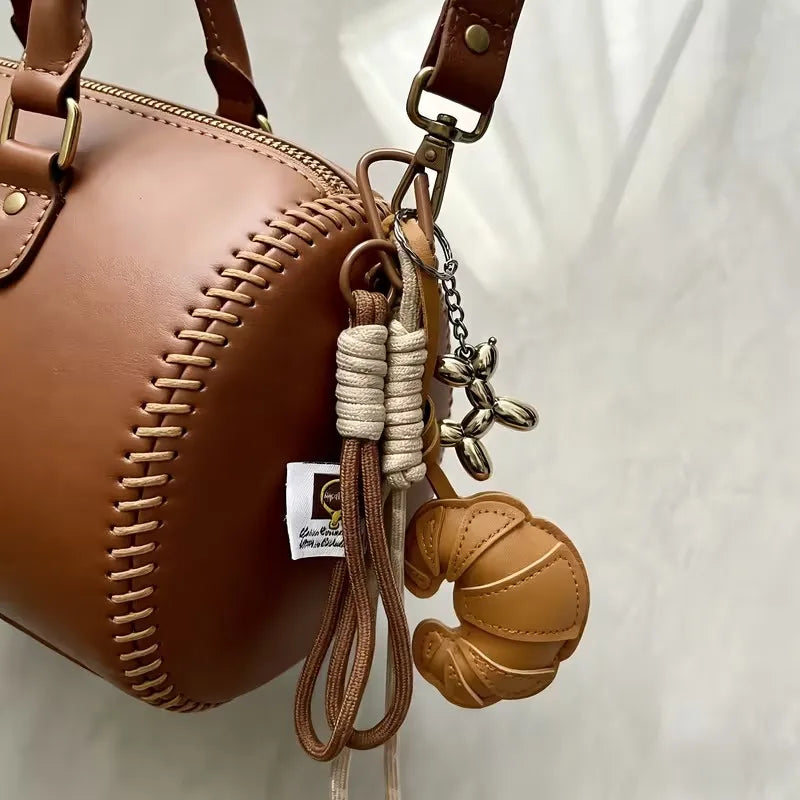 A brown leather handbag with a braided detail and a croissant-shaped keychain attached.