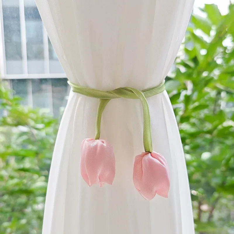 A set of pink tulip curtain tie backs with light green fabric straps hanging from a white drape.