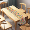 A light wood table is set with a colorful Day of the Dead Mexican Fiesta table runner featuring floral patterns.