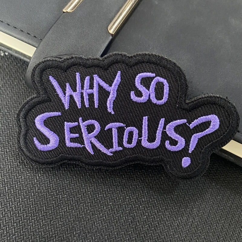 A black embroidered patch with purple text that reads Why So Serious?