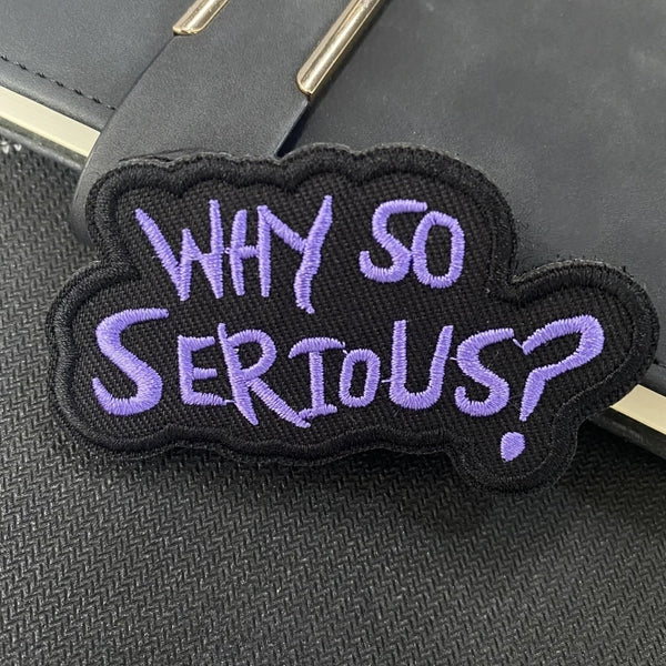 A black embroidered patch with purple text that reads Why So Serious?