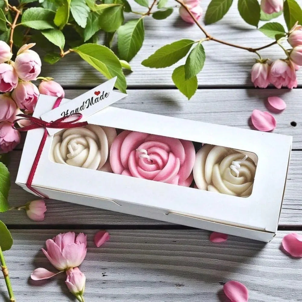A white box containing three silicone rose flower molds in shades of pink and cream, set against a wooden background with gre