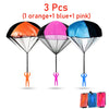 Three colorful hand-thrown parachute toys in orange, blue, and pink are displayed against a white background.
