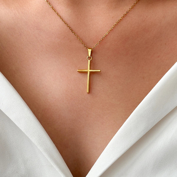 A gold stainless steel cross pendant necklace is displayed against a light skin tone and white shirt collar.