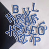 A collection of blue and white embroidered alphabet letters including B, L, H, R, V, X, W, Z, E, I, P, and O.