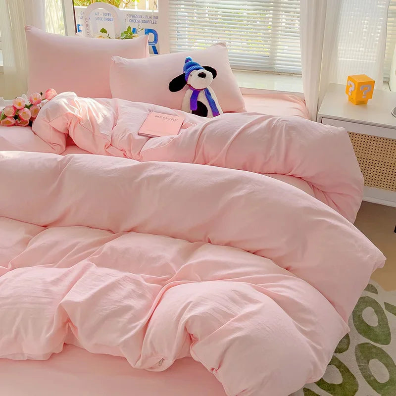A pink cotton bedding set featuring a flat sheet, duvet cover, and pillowcases with a black and white character pillow.