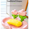 Pink floral shaped soap dish with a yellow bar of soap and green stems on a white surface.