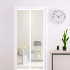A framed mirror reflects a room with a lamp and a round clock on a white wall.