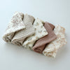 A stack of soft cotton gauze burp cloths featuring floral patterns in neutral tones.
