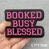 Black embroidered patch with pink text reading BOOKED BUSY BLESSED shown in a hand.