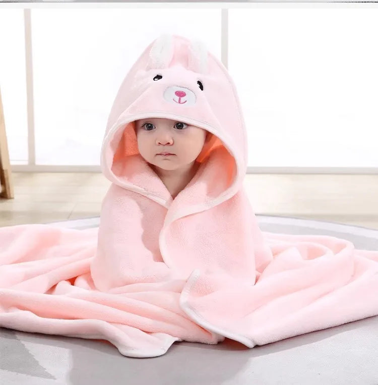 A pink fuzzy hooded baby bathrobe towel with a cartoon bunny face is draped on a white surface.