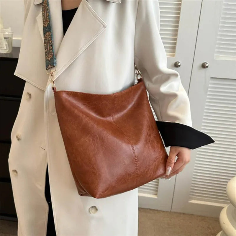 A woman holds a brown leather shoulder bag with golden embroidery against a white coat.