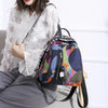 A woman wearing a white sheer blouse and gray pants is holding a purple and green patterned backpack.
