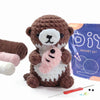 A brown crocheted teddy bear with a pink plant accessory is shown next to its purple kit packaging and crochet tools.