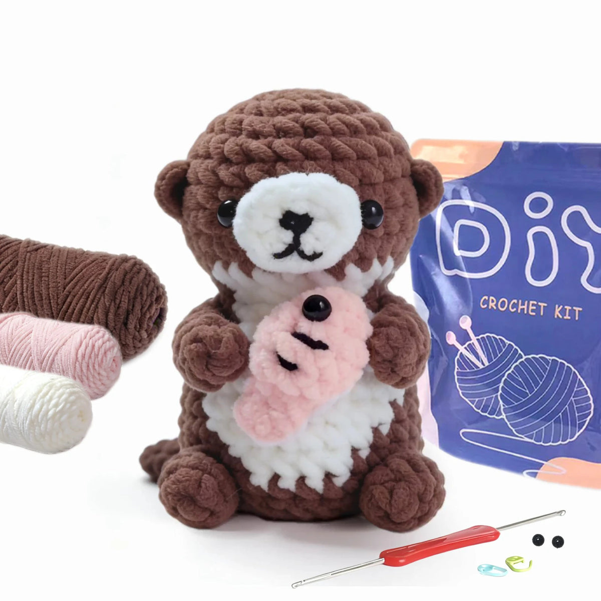 A brown crocheted teddy bear with a pink plant accessory is shown next to its purple kit packaging and crochet tools.