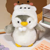 A white and gray penguin plush toy wearing a white hat sitting on a white surface.