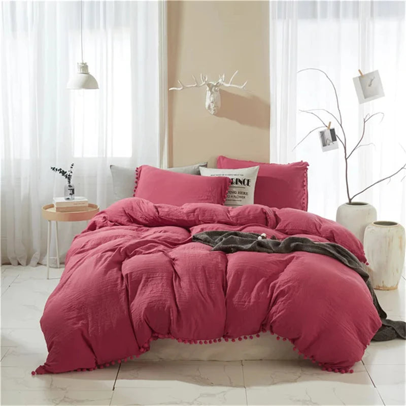 A pink duvet cover set with pom tassels is displayed on a bed in a bright room.
