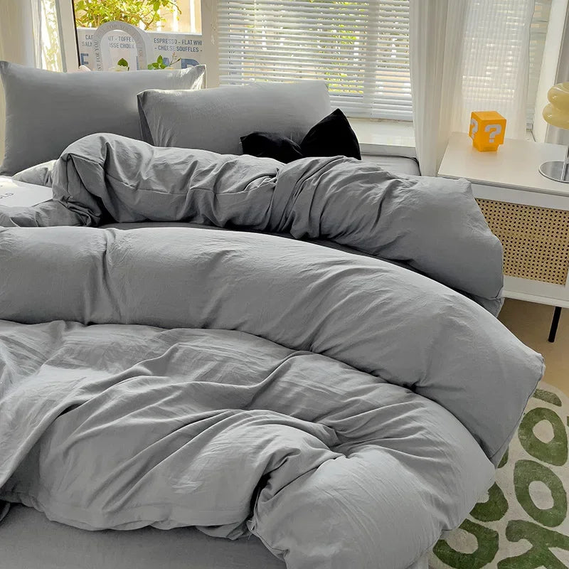 A gray cotton bedding set featuring a flat sheet, duvet cover, and pillowcases displayed on a bed.