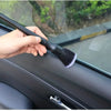 A hand is using a black soft bristle detailing brush on the interior surface of a car door panel.