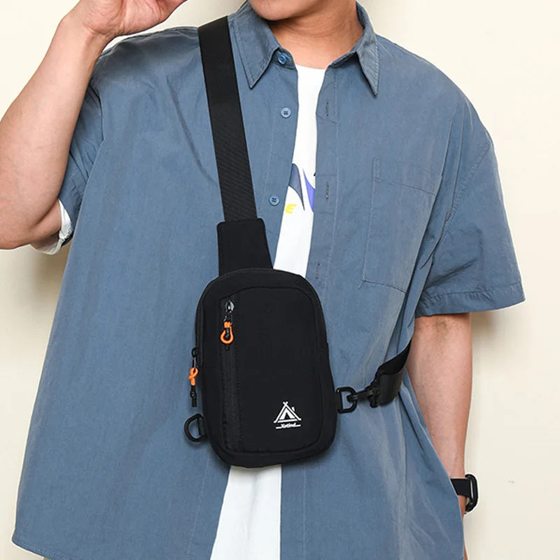 A person wearing a light blue shirt is holding a black water-resistant nylon chest sling bag.