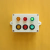 A white plastic board with six colored buttons and switches mounted on a yellow background.