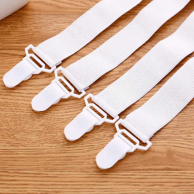 A set of four white adjustable bed sheet holder clips lying on a wooden surface.
