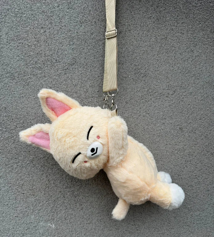A light yellow plush toy resembling a dog or puppy with closed eyes and pink inner ears hanging from a strap.