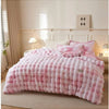 A pink checkered plush winter comforter draped on a bed with light wood accents and sheer curtains.