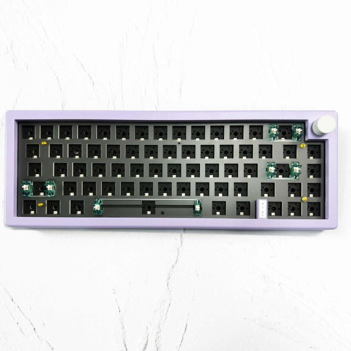 Teclado mecánico de 67 teclas púrpura con iluminación RGB y perilla de volumen sobre una superficie de mármol blanco.