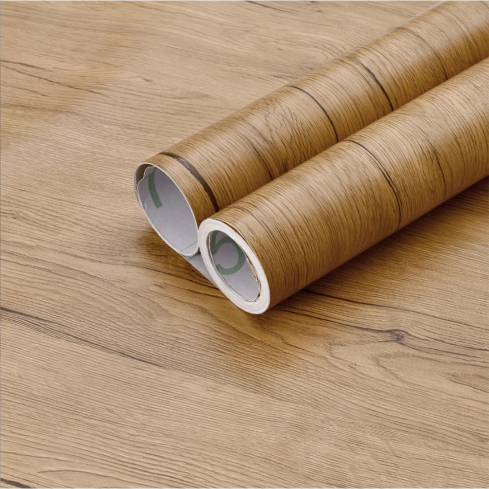 Two rolls of self-adhesive wood grain waterproof wallpaper lying on a wooden surface.