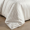 A white satin striped jacquard duvet cover set draped on a bed.