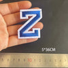 A hand holds a blue embroidered letter N patch, measuring 5 by 36 centimeters.
