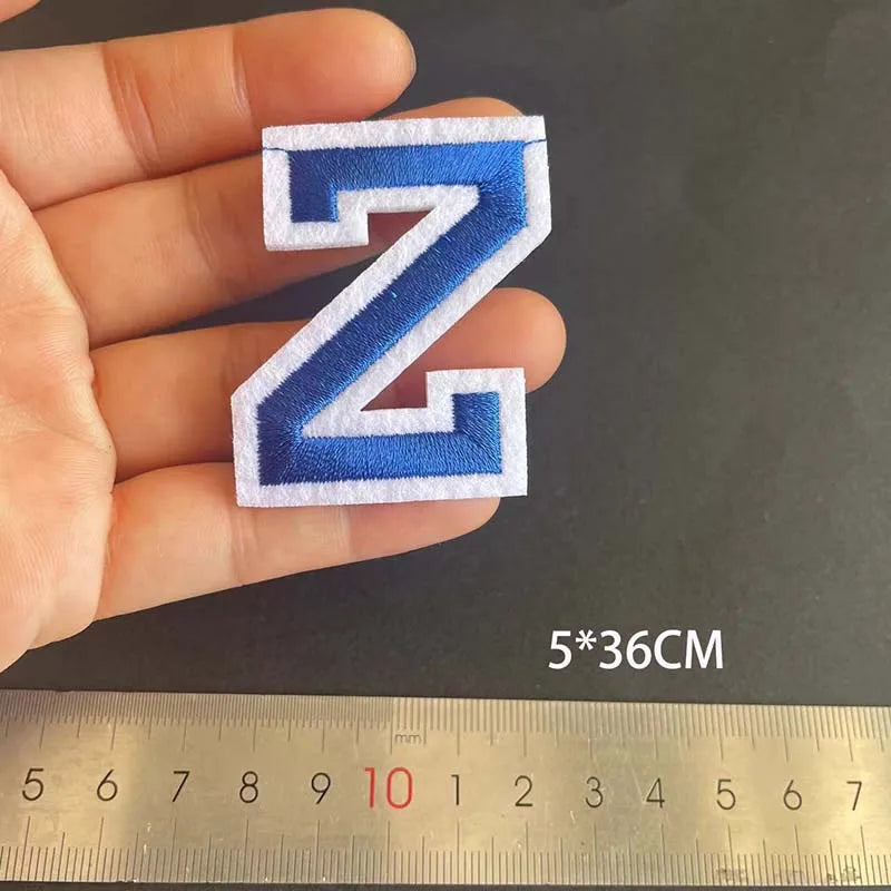 A hand holds a blue embroidered letter N patch, measuring 5 by 36 centimeters.